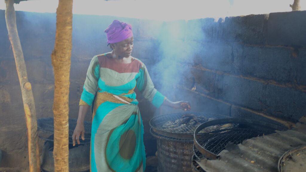 A Nigerian woman standing over a fish smoker made from an oil drum.
